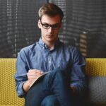 Person in Blue Denim Jacket Sitting on Chair While Writing